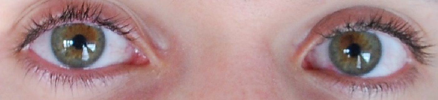 Gros plan sur deux yeux verts aux cils maquillés de mascara noir, avec des paupières légèrement rosées.